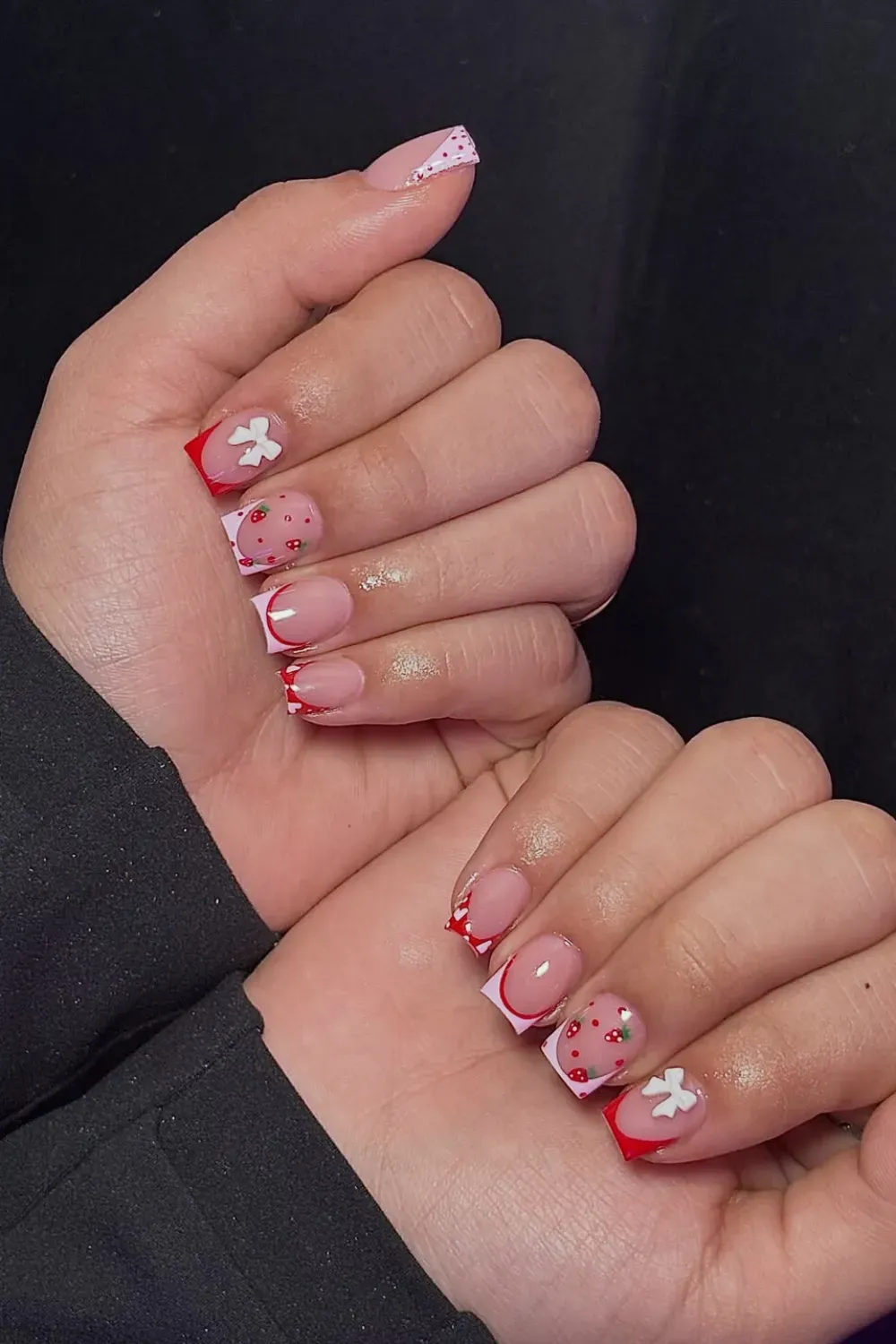 Short square nails with red and checkerboard French tips, featuring hand-painted strawberries and a white bow accent.
