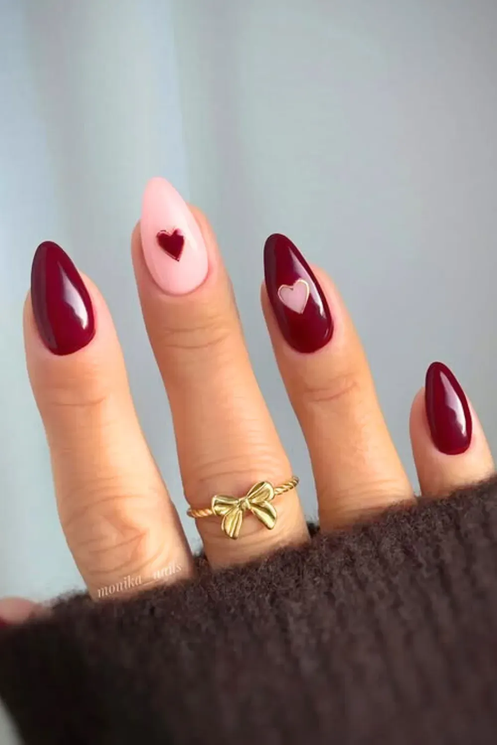 Almond-shaped nails with glossy burgundy bases and two light pink accent nails featuring small burgundy hearts.