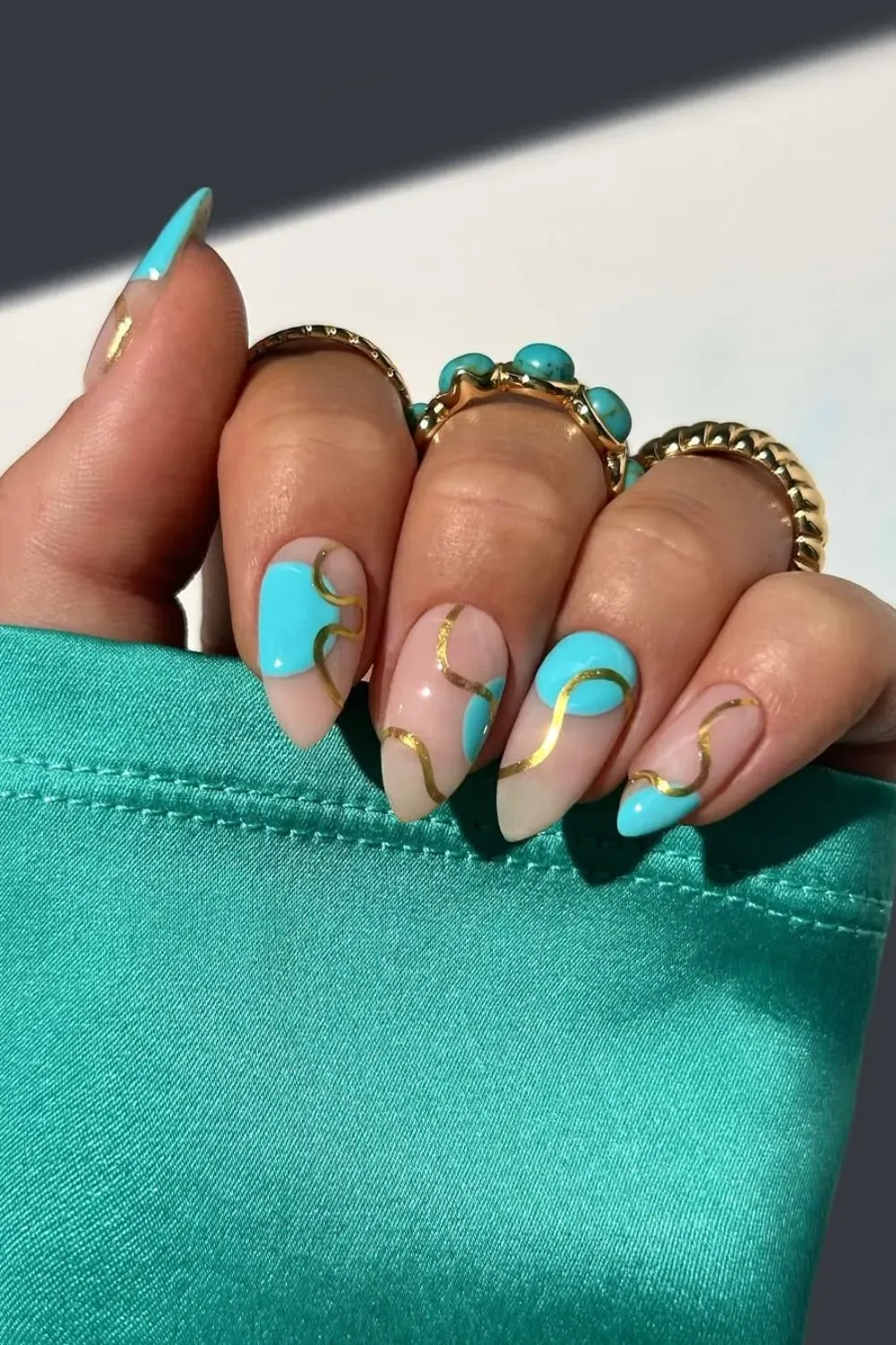 Teal and gold foil nail art on almond-shaped nails.