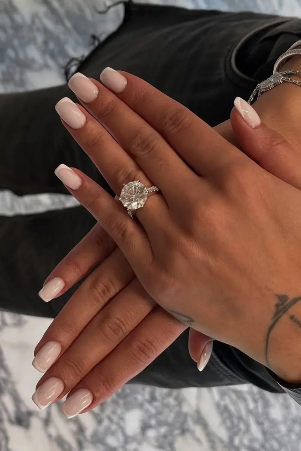 Elegant short square nails with a soft pink base and thin white French tips, featuring a large diamond ring.