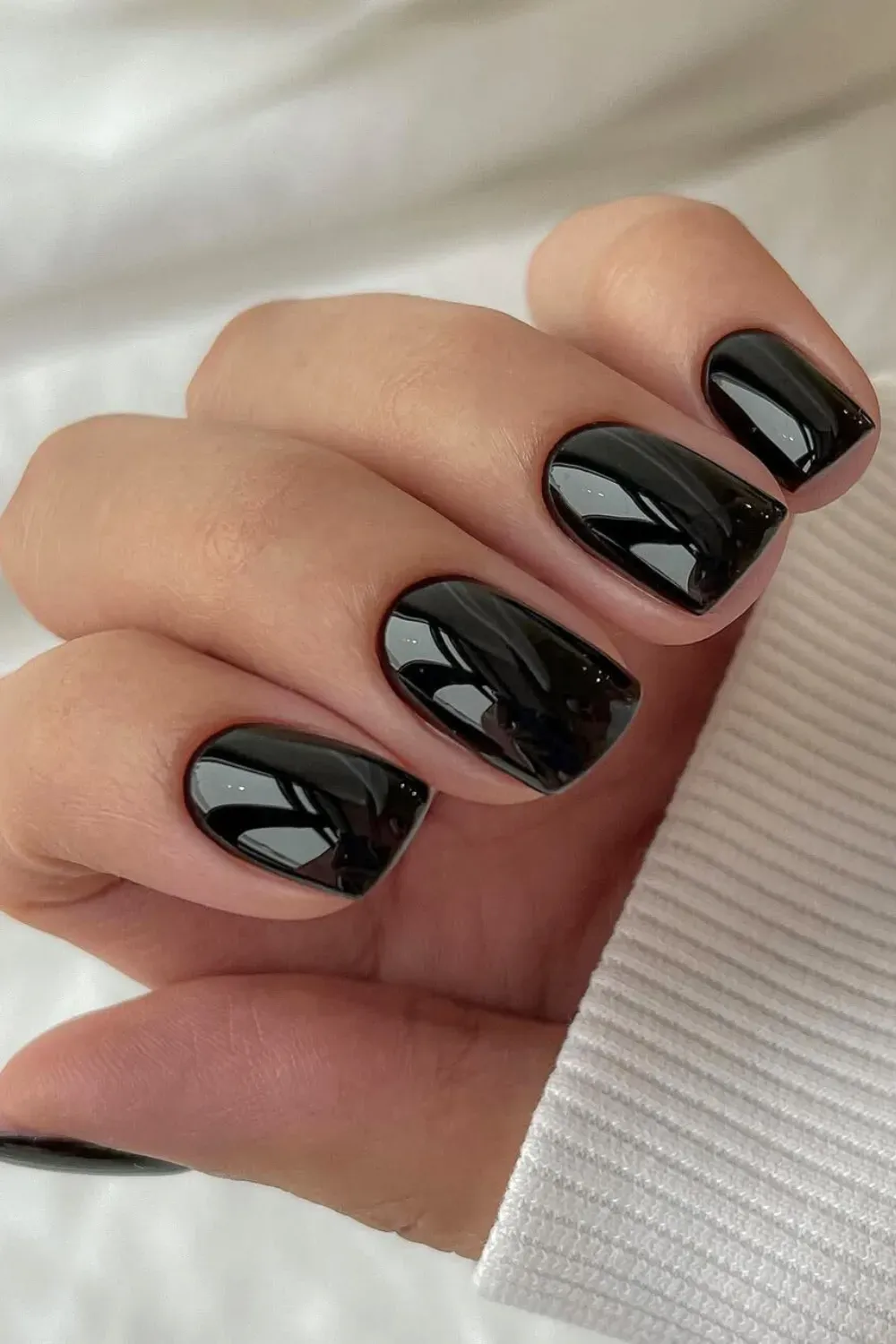 Close-up of a hand with neat, square-shaped nails painted in a solid, high-shine jet black polish.