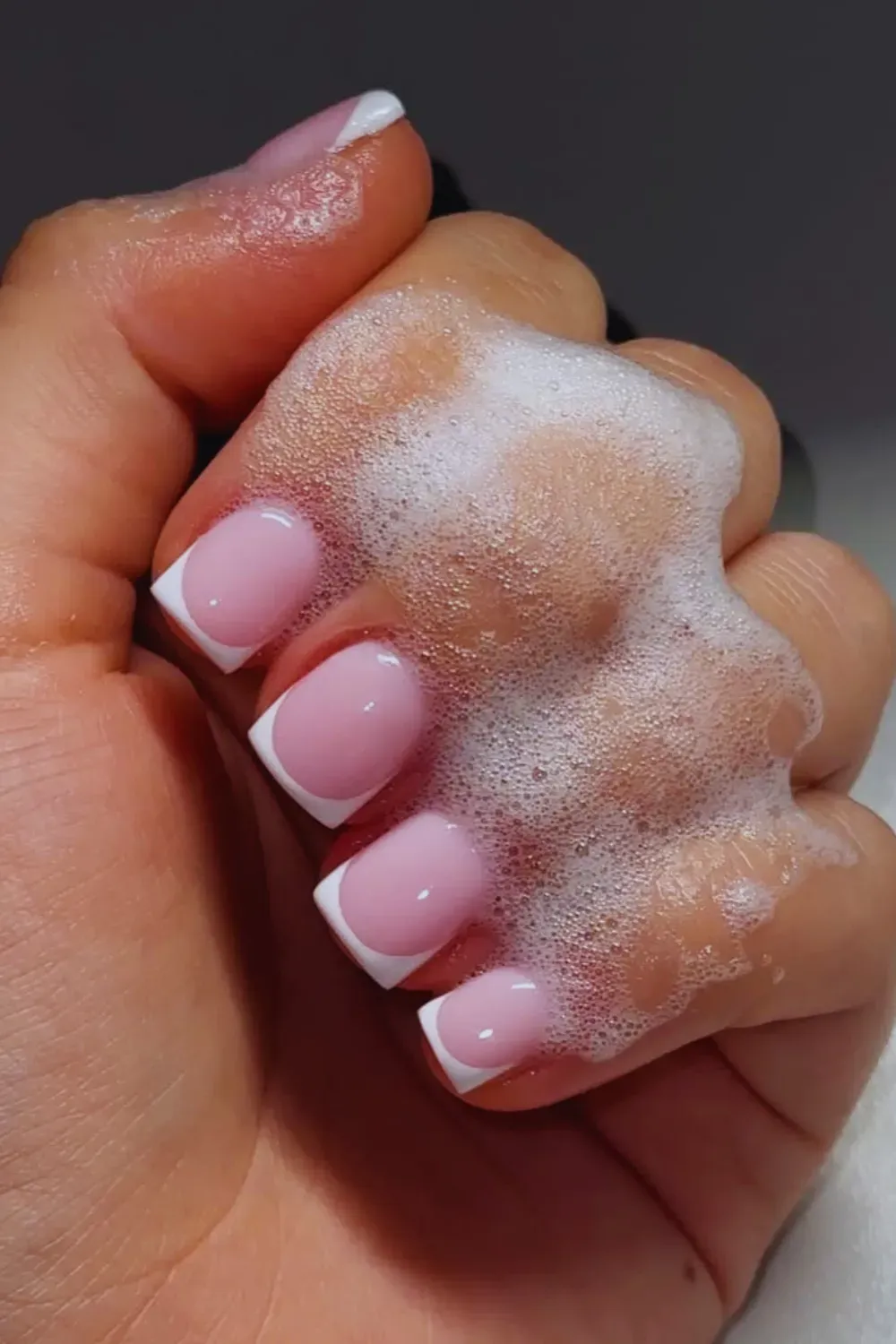 Short square nails with a perfect, glossy, classic white French tip on a milky pink base, shown while washing hands