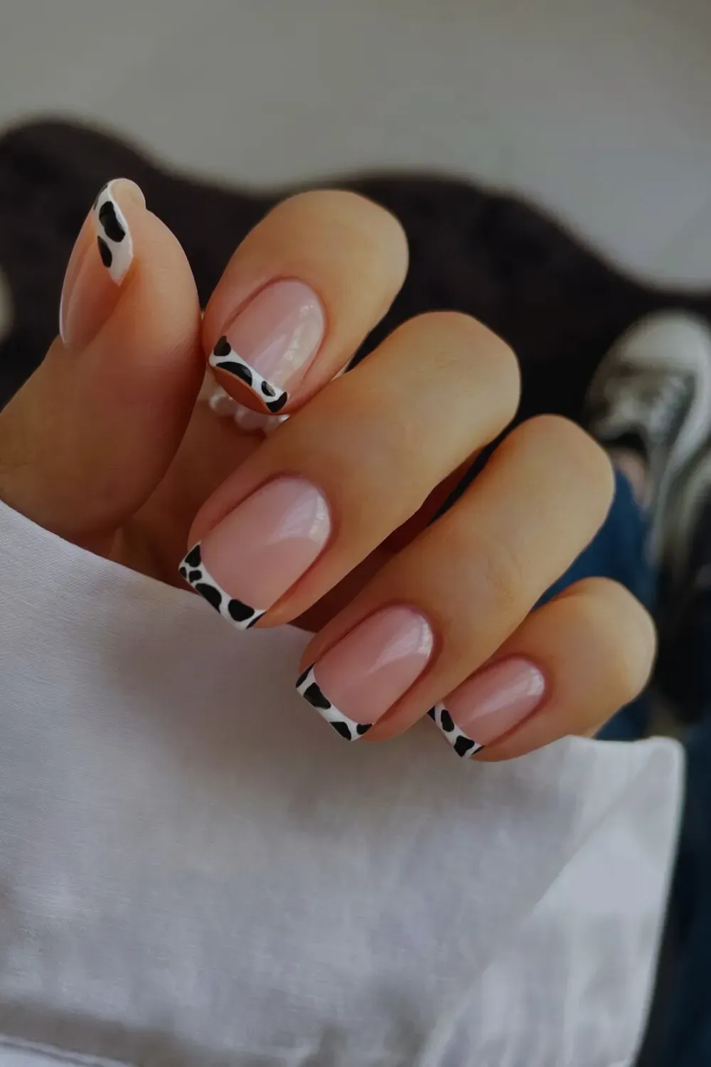 Square nails with a nude base and black and white cow print on the French tips.