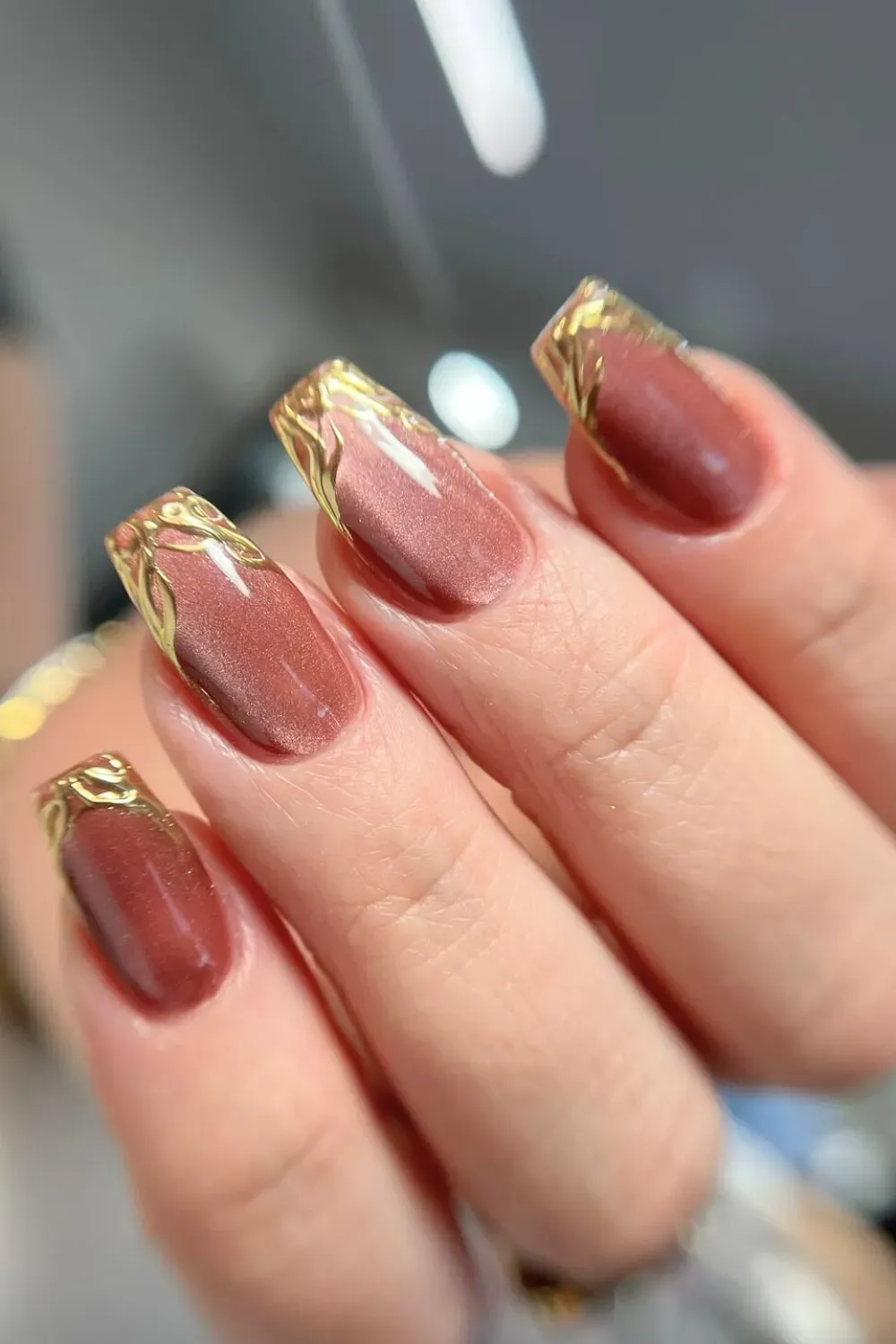 Bronze Cat Eye French Nails Alt Text: Square nails with bronze cat eye french tip and gold chrome swirls.