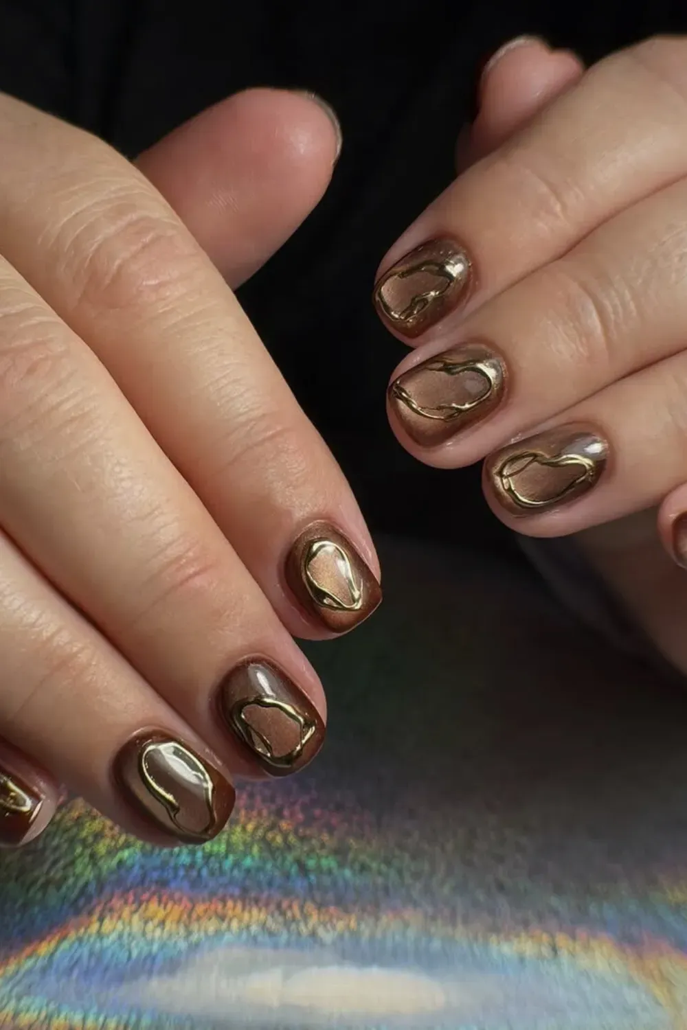 Close up of short dark brown magnetic nails with abstract gold chrome outlines