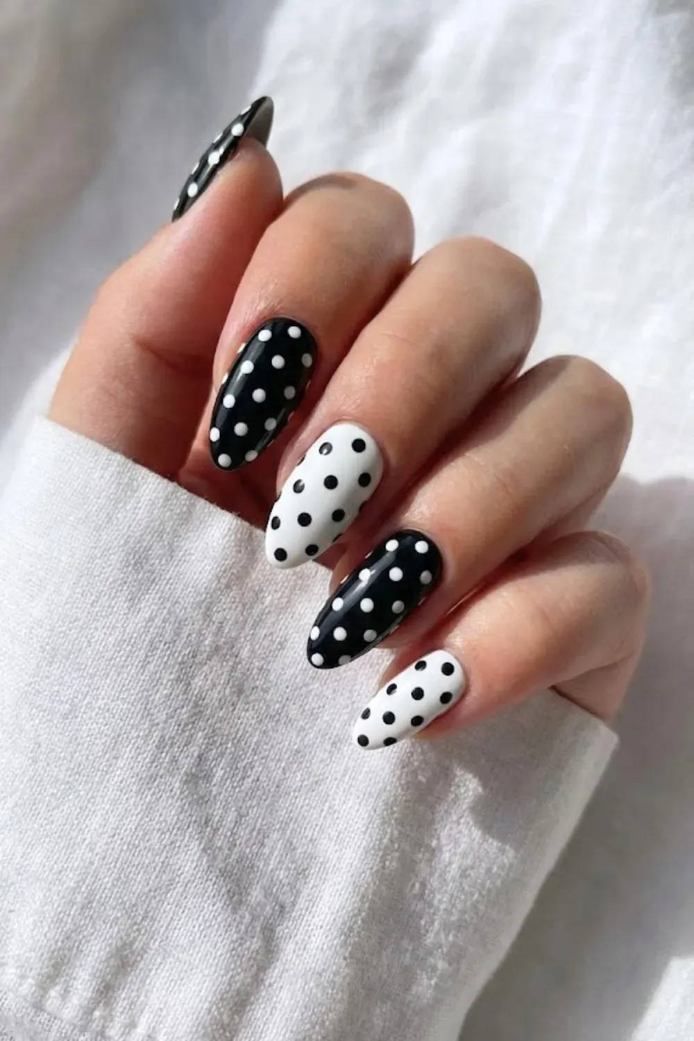 Black and White Mix Match Polka Dot Nails - Almond nails featuring alternating black bases with white dots and white bases with black dots against a white shirt.