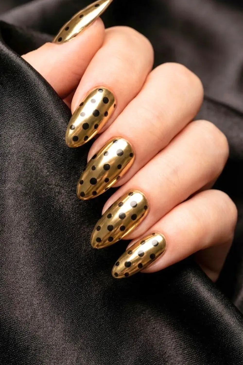Gold Chrome and Black Polka Dot Nails - Luxurious long almond nails with a reflective gold chrome finish and black polka dots against dark silk.