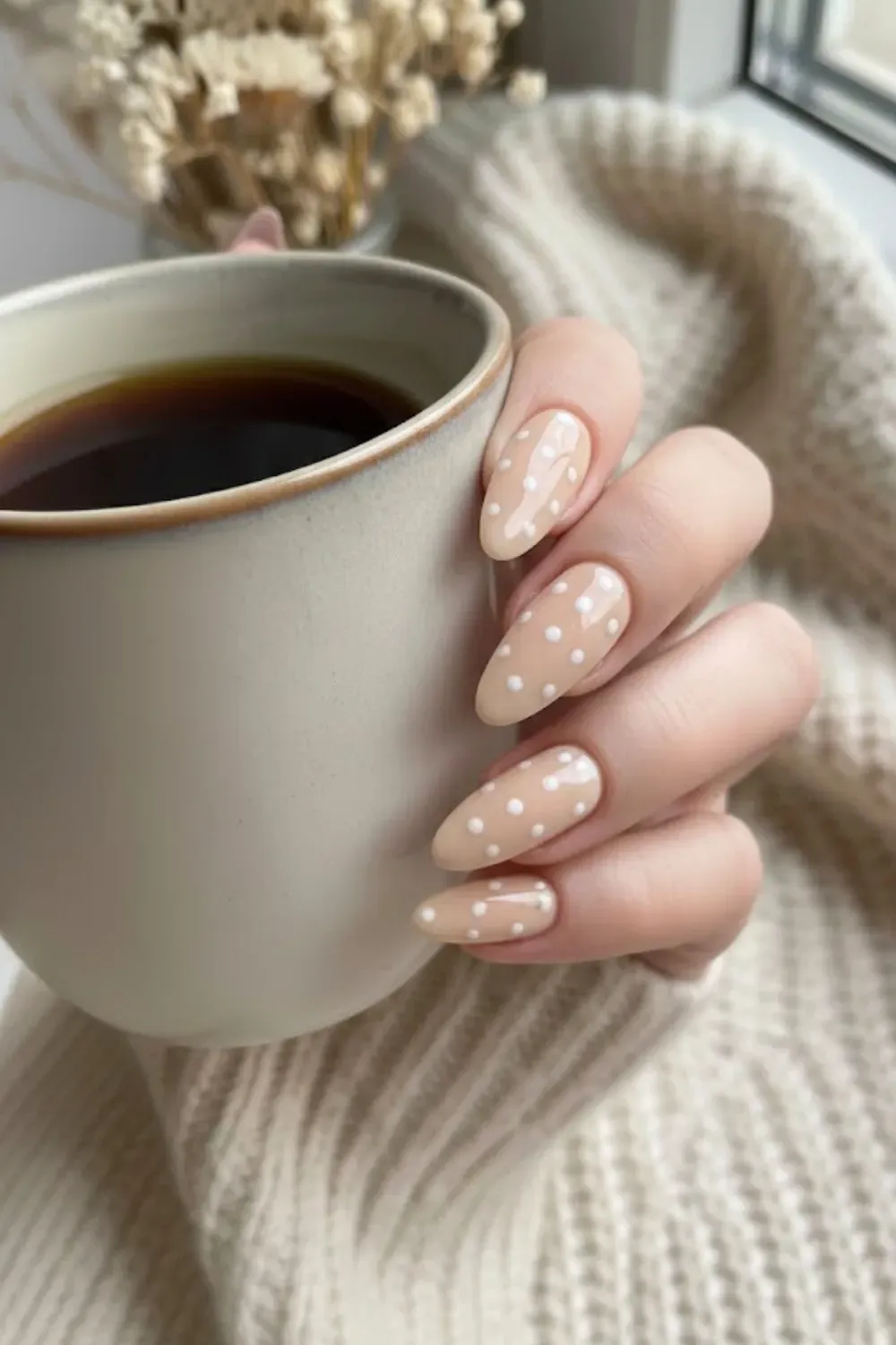 Minimalist Nude and White Polka Dot Nails - Simple almond nails with a glossy nude base and delicate white polka dots holding a beige mug.