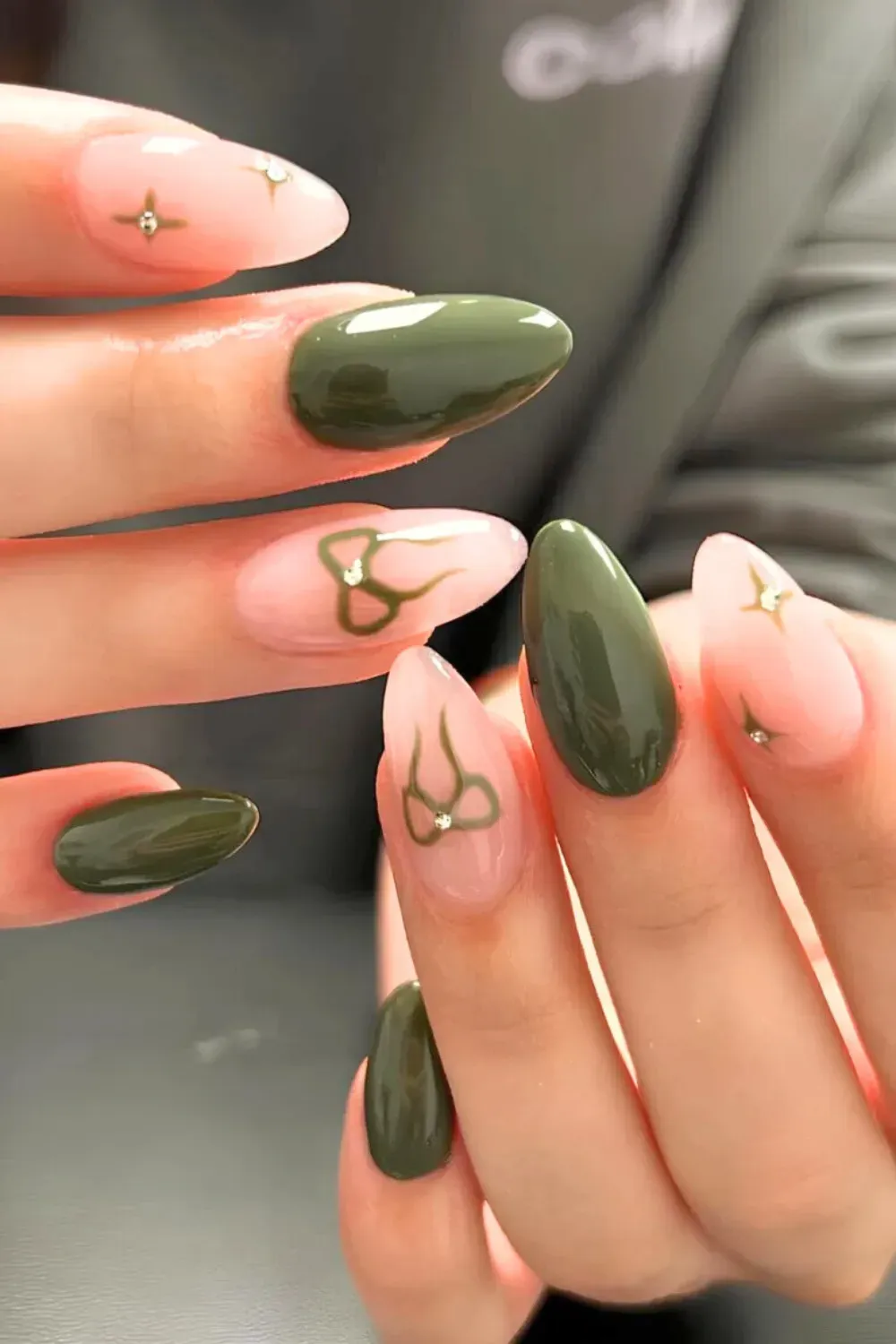 Olive Green Bow and Gem Almond Nails - Long almond nails alternating between solid olive green and sheer pink with olive bow decals and gem accents.