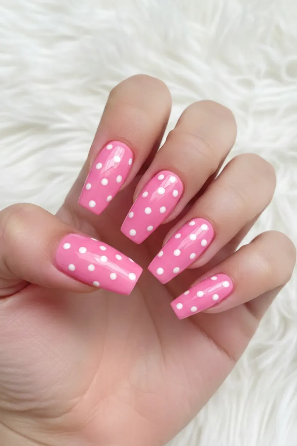 Hot Pink and White Polka Dot Coffin Nails - Long coffin-shaped nails painted glossy hot pink with crisp white polka dots against a white fur background.