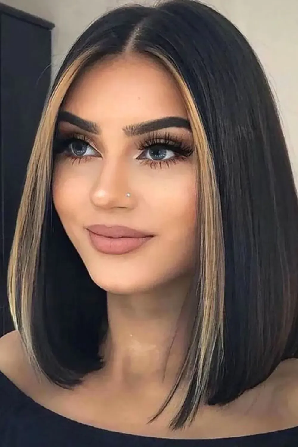 Black Bob with Bold Caramel Money Piece	Woman with a sleek, straight black bob featuring striking chunky blonde face-framing highlights.