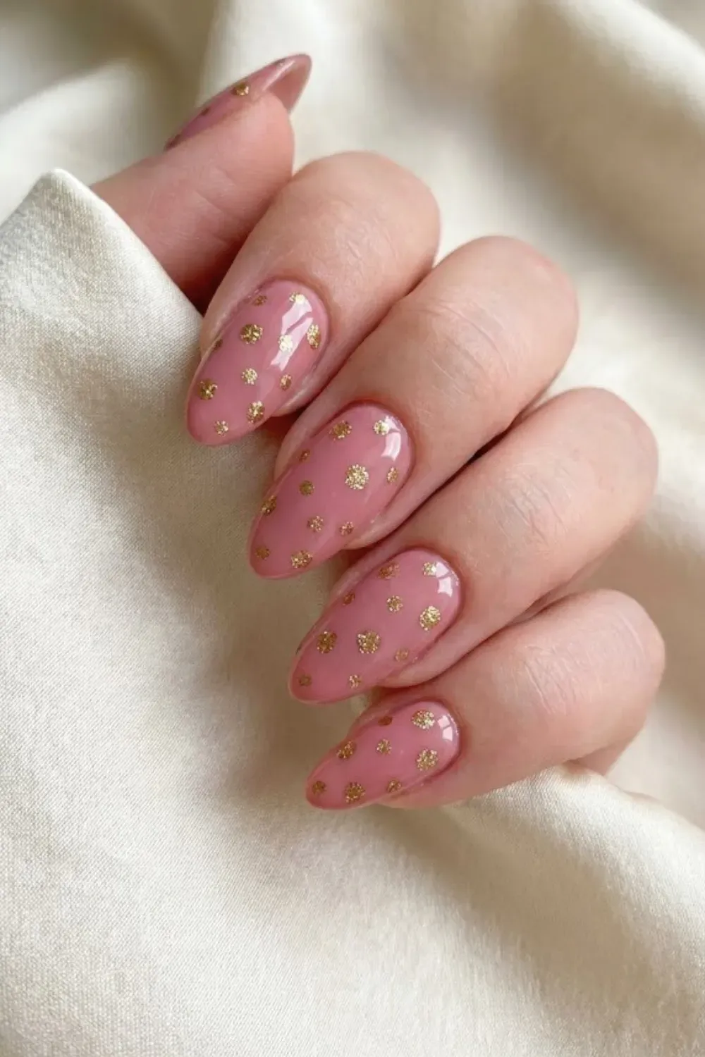Dusty Rose and Gold Glitter Polka Dot Nails - Oval nails in a sheer dusty rose pink featuring sparkling gold glitter polka dots rests on silk fabric.