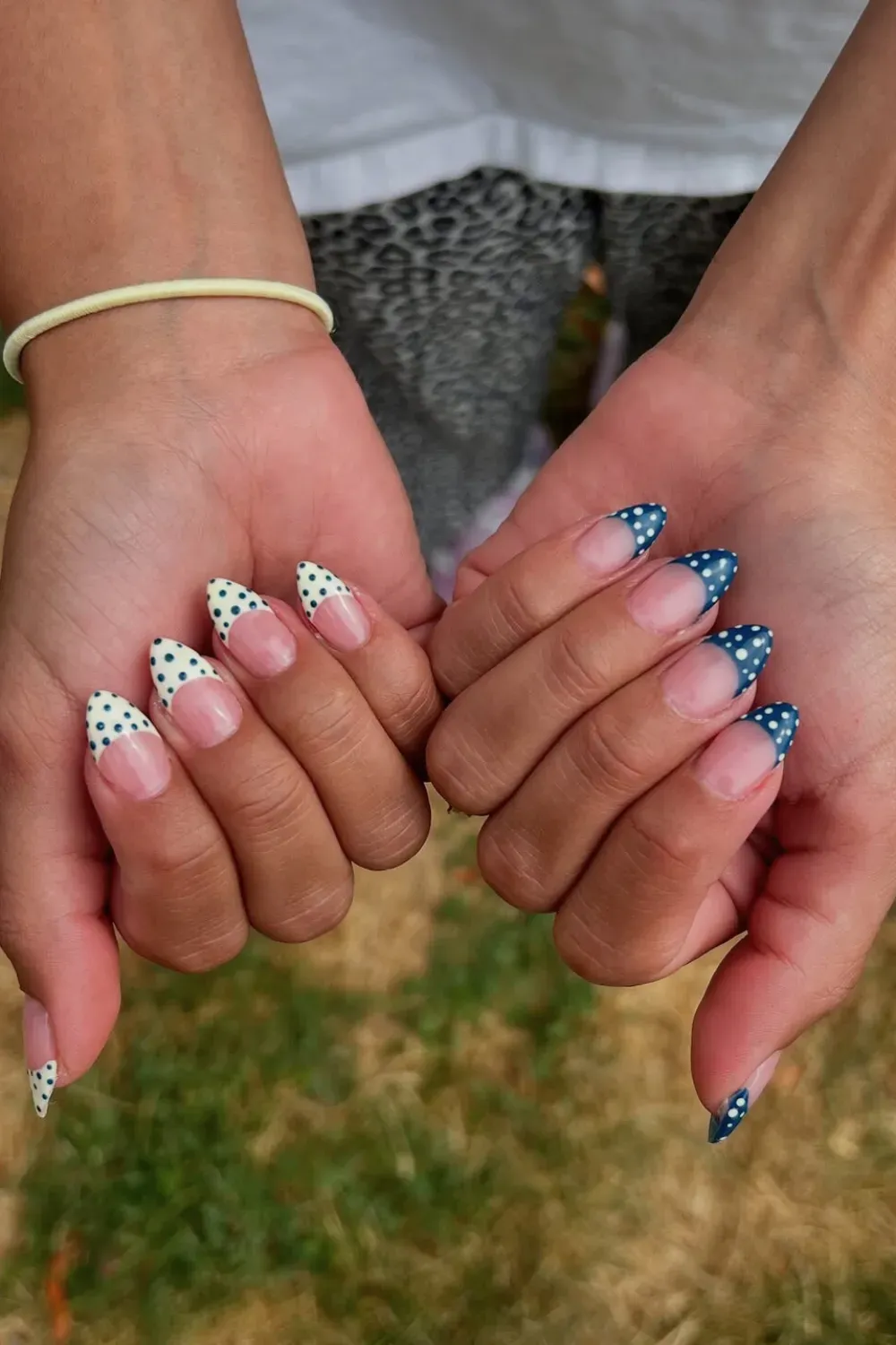Blue French Tip Polka Dot Nails - Hands showing almond nails with a natural pink base and dark blue french tips covered in white polka dots.