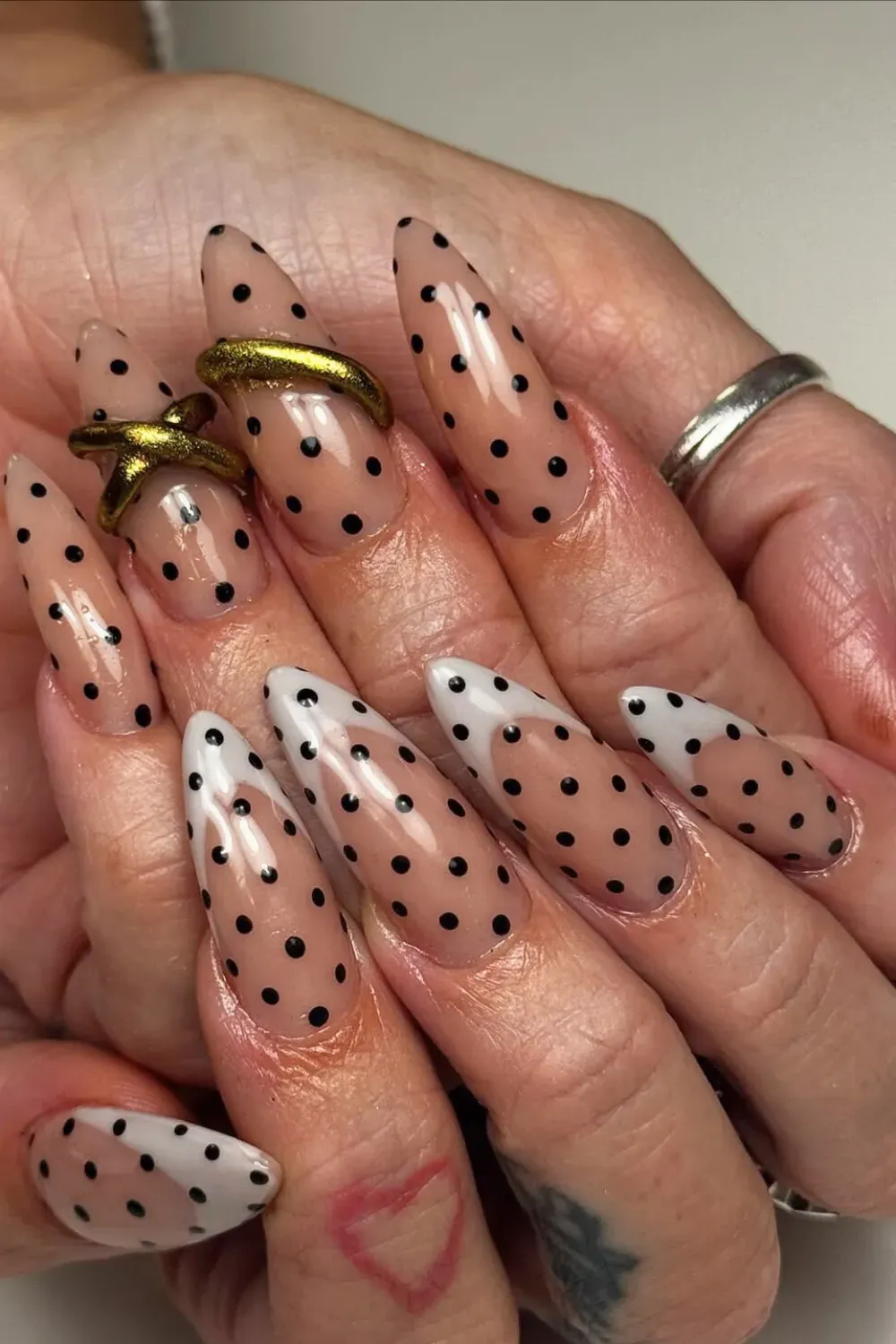 Long Stiletto Nude and Black Polka Dot Nails - Very long stiletto nails with a sheer nude base and sparse black polka dots, accented with gold rings.