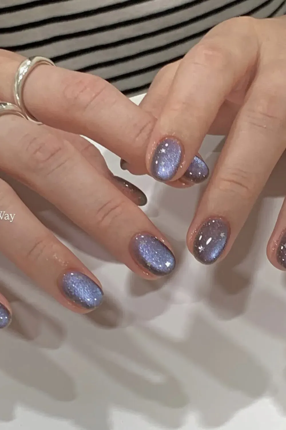 Periwinkle blue cat eye nails with tiny white star decals on short oval nails.