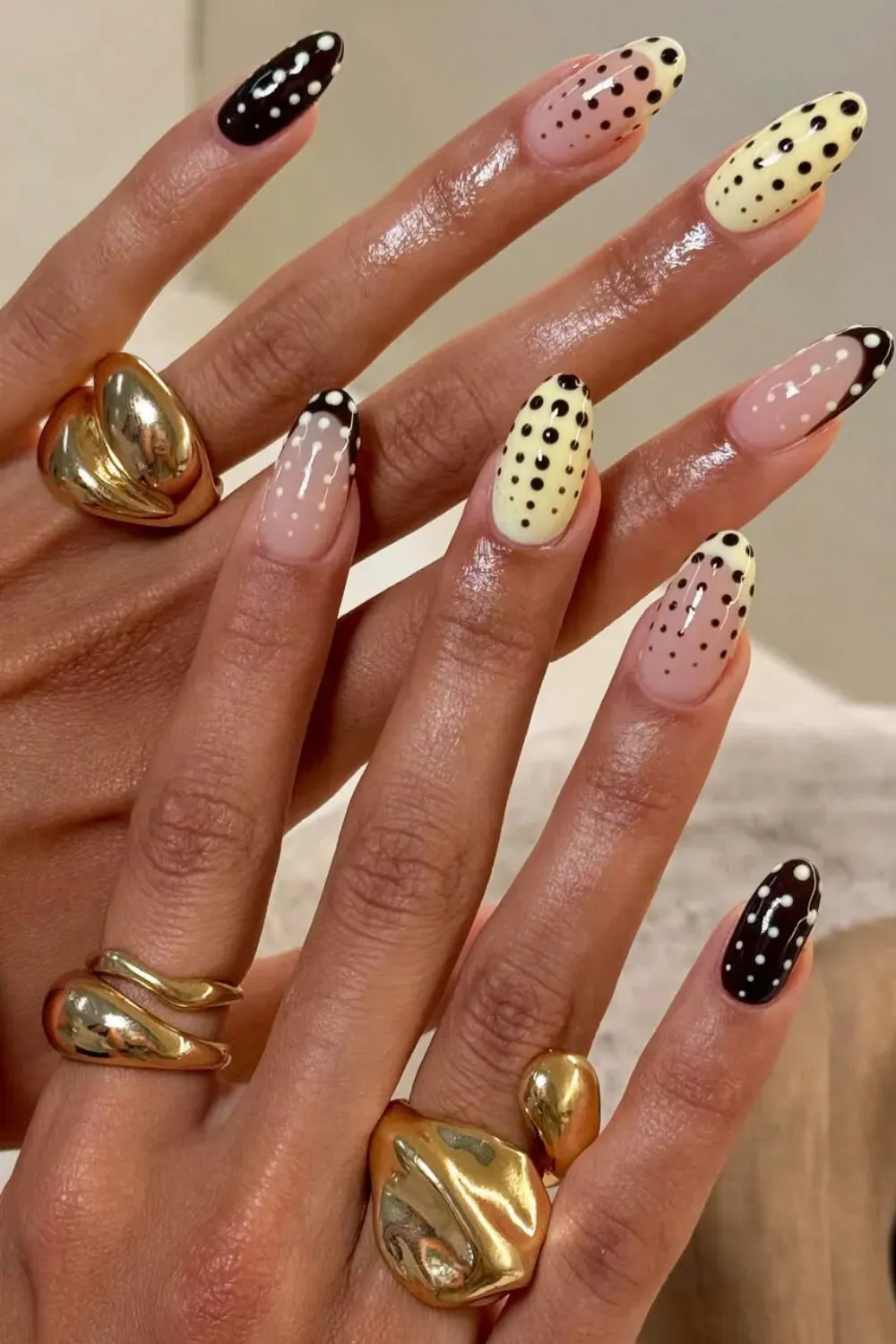 Abstract Nude and Black Polka Dot Mix Nails - Oval nails displaying a variety of black and nude abstract designs, lines, and varied polka dot patterns with gold rings.