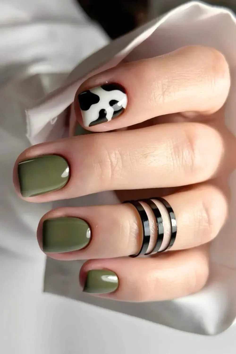 Olive Green Nails with Cow Print Accent - Short square nails painted solid olive green with one accent nail featuring a black and white cow print.