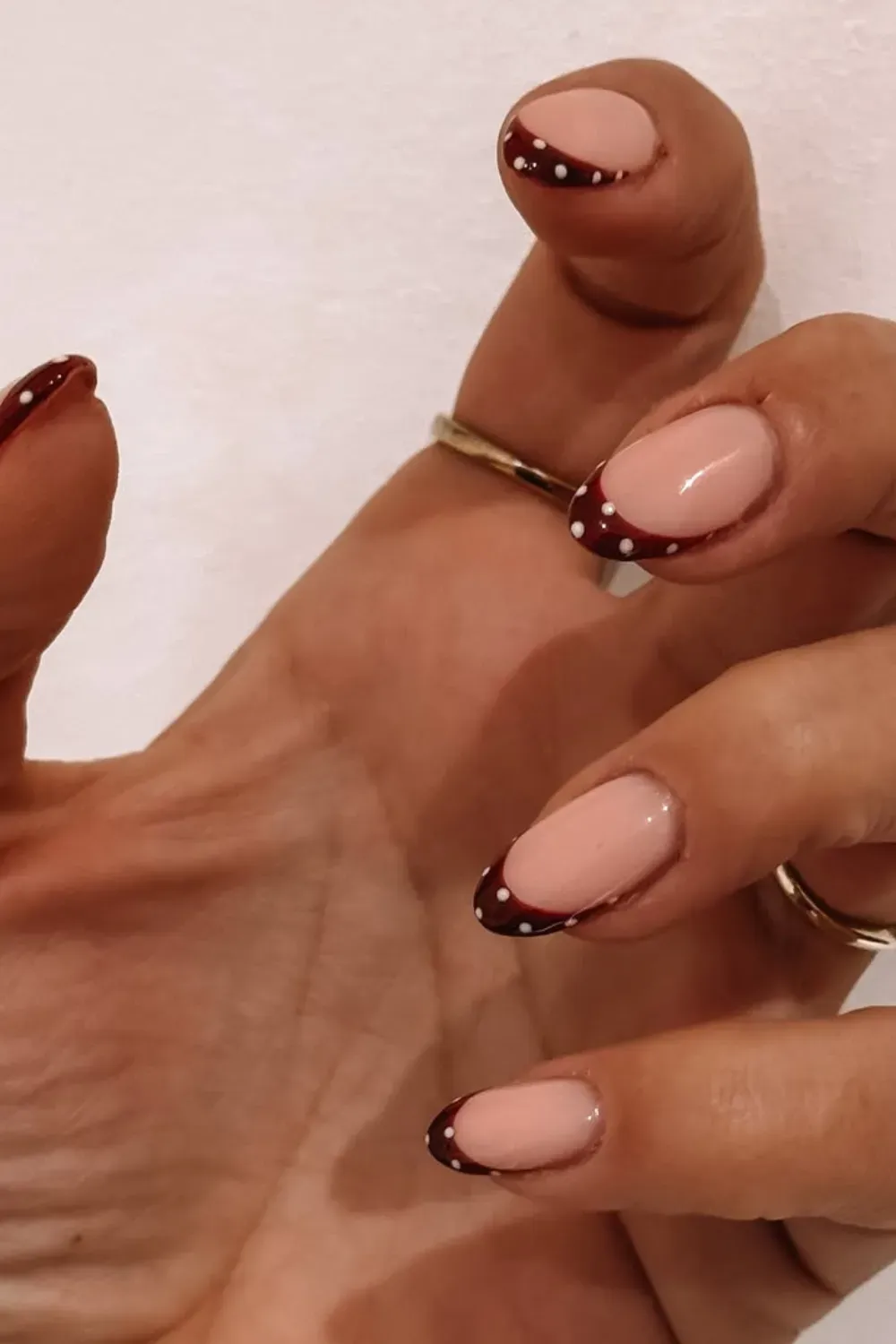 Deep Red Micro French Polka Dot Nails - Hand reaching out showing oval nails with a sheer nude base and very thin, deep red french tips dotted with white.