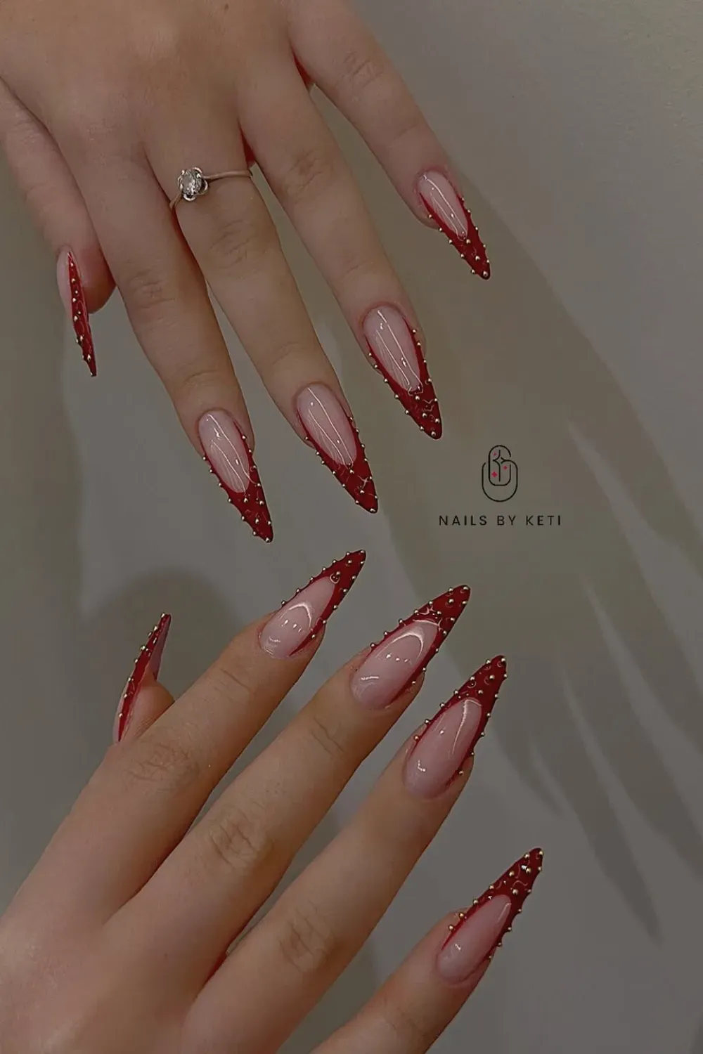 Red Stiletto French With Gold Studs Alt Text: Long stiletto nails with red french tip and gold beaded lining.