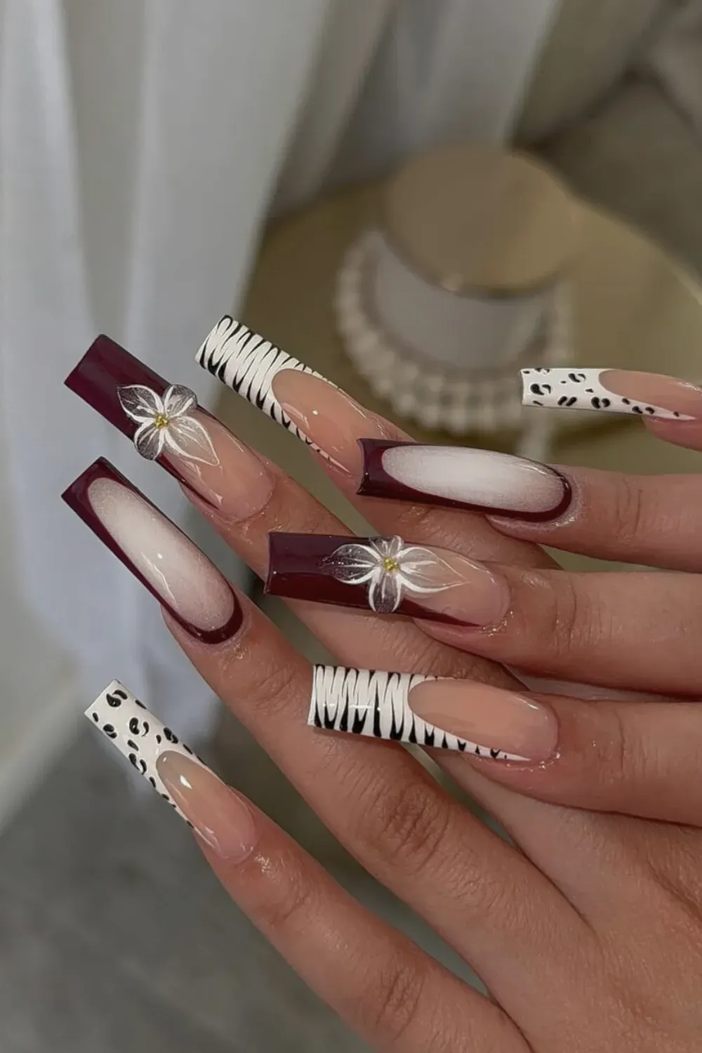 Burgundy Zebra French Nails Alt Text: Dark red french tips with zebra print and white 3D flower accent.