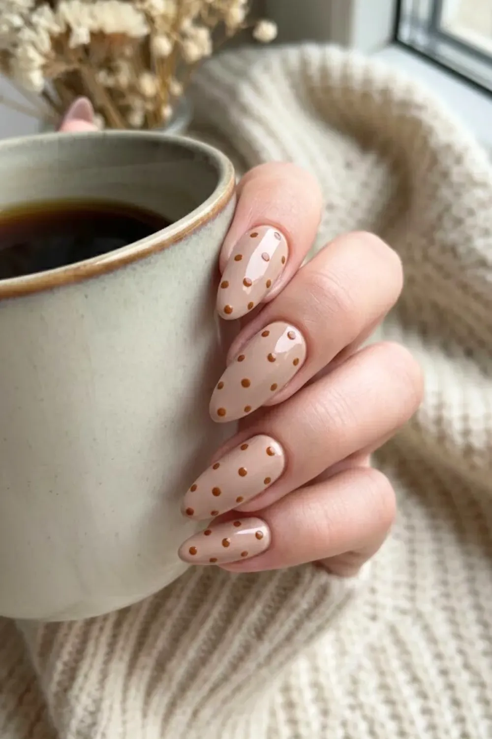 Cozy Latte Polka Dot Nails - Close up of almond-shaped nude nails with warm brown polka dots holding a ceramic coffee cup.
