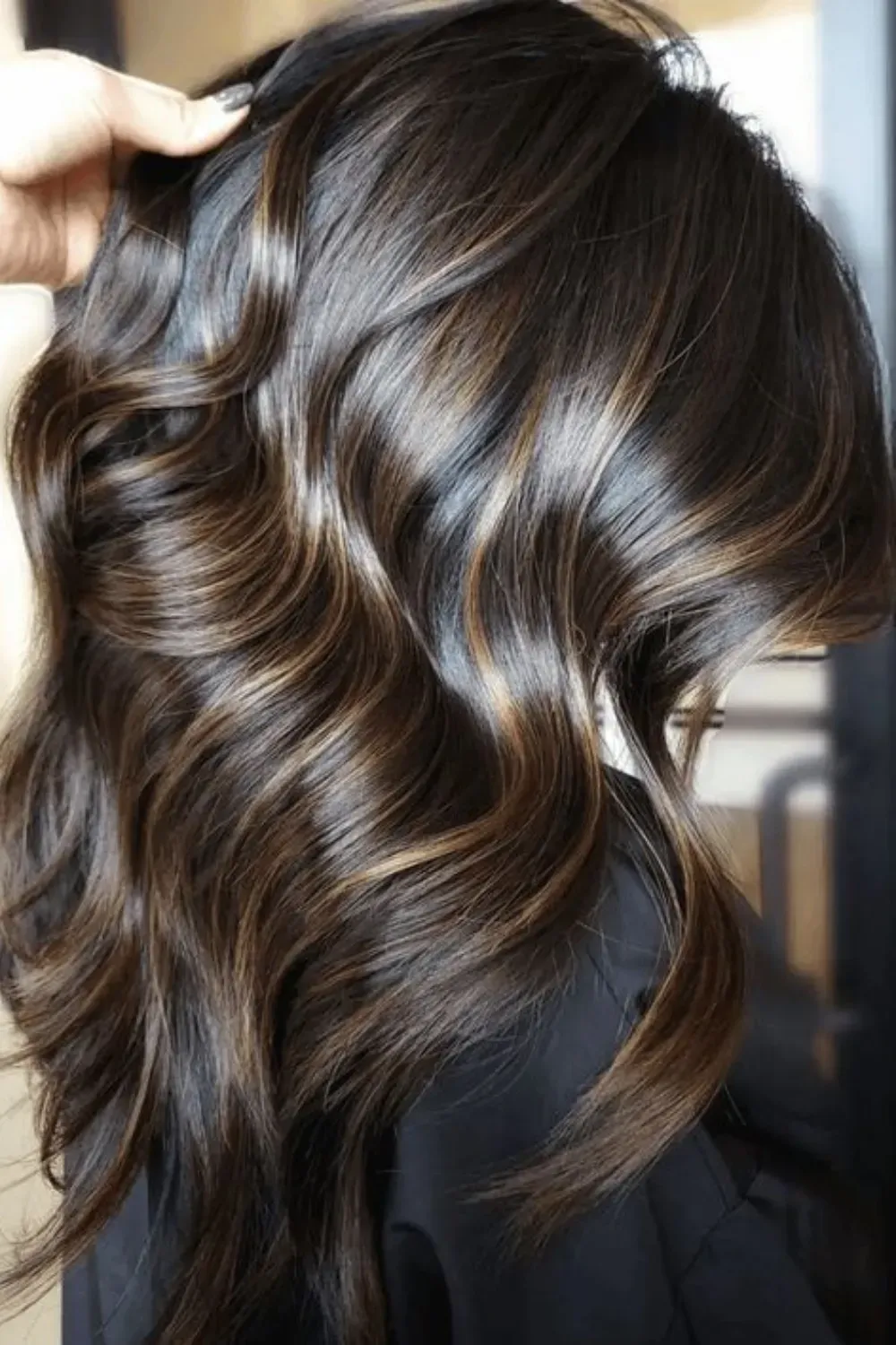 High-Shine Wavy Hair with Subtle Caramel Streaks	Side view of dark, wavy hair with finely placed, high-shine caramel highlights.