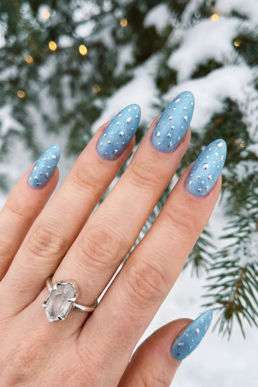 Metallic Blue and Silver Polka Dot Nails - Textured metallic baby blue almond nails with raised silver metallic polka dots against snowy pine branches.