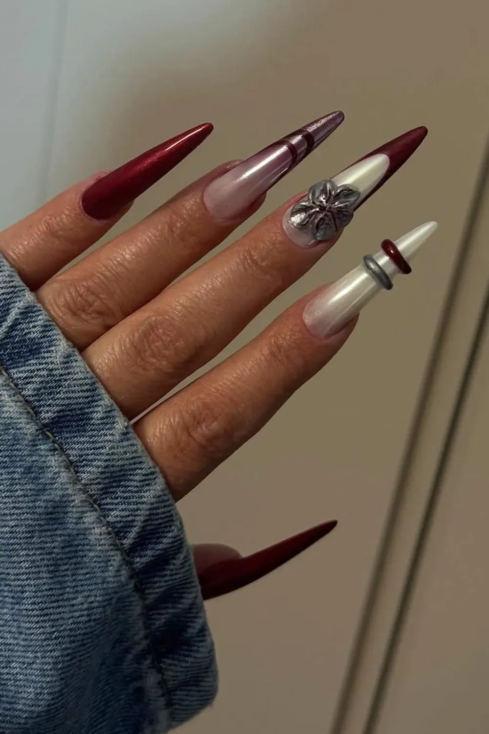 Extreme stiletto nails featuring glossy blood-red, pearl white, a silver 3D flower, and metallic rings.
