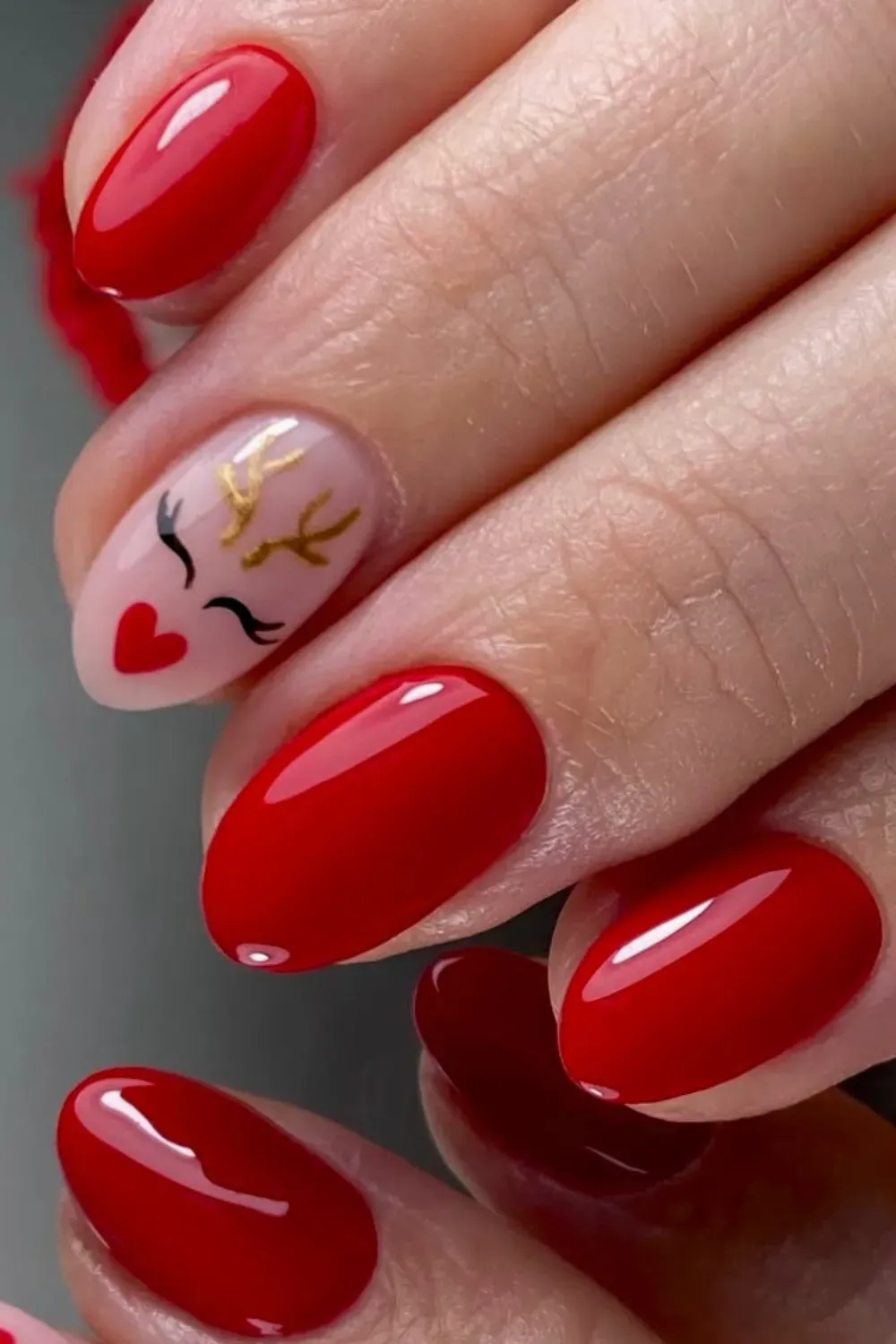 Red Nails with Reindeer Face Art - Oval red nails with a cute hand-painted reindeer face with gold antlers on the accent nai