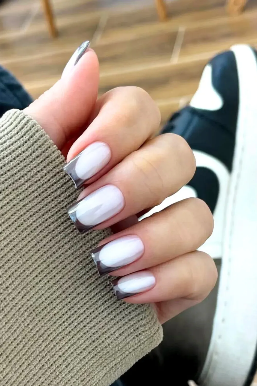 Glazed Dark Tip French Manicure	Hand in a tan sleeve showing long, square nails with a milky base, dark tips, and a pearl/chrome finish