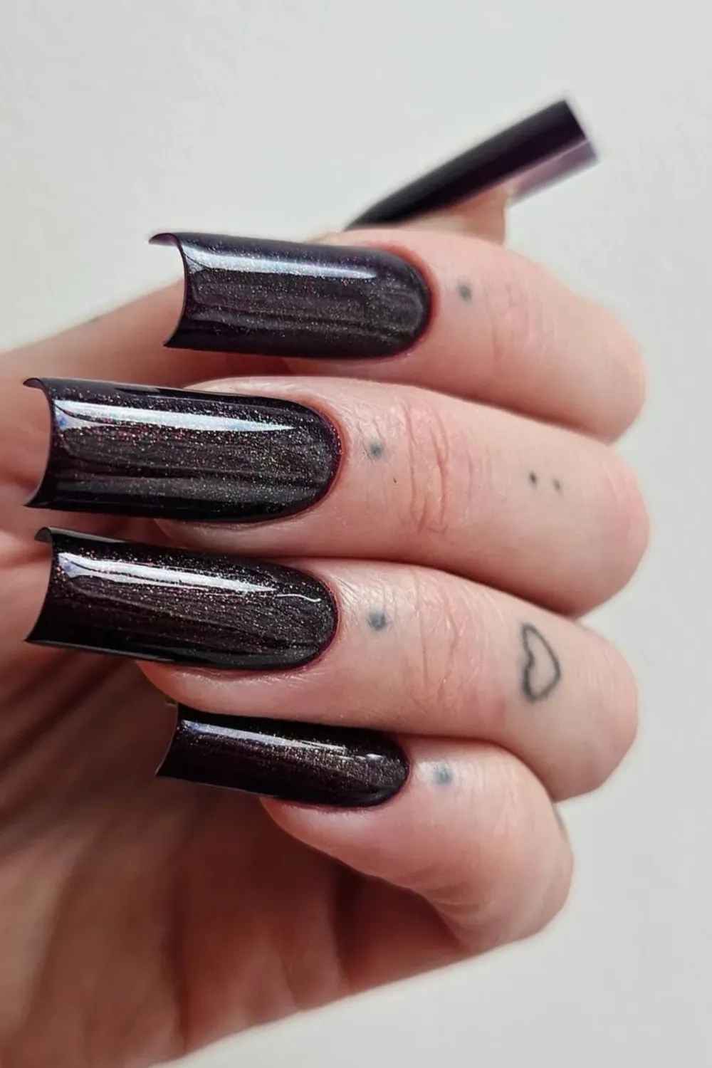 Extra-long trapezoid nails in a deep black polish with multi-colored holographic glitter shimmer.