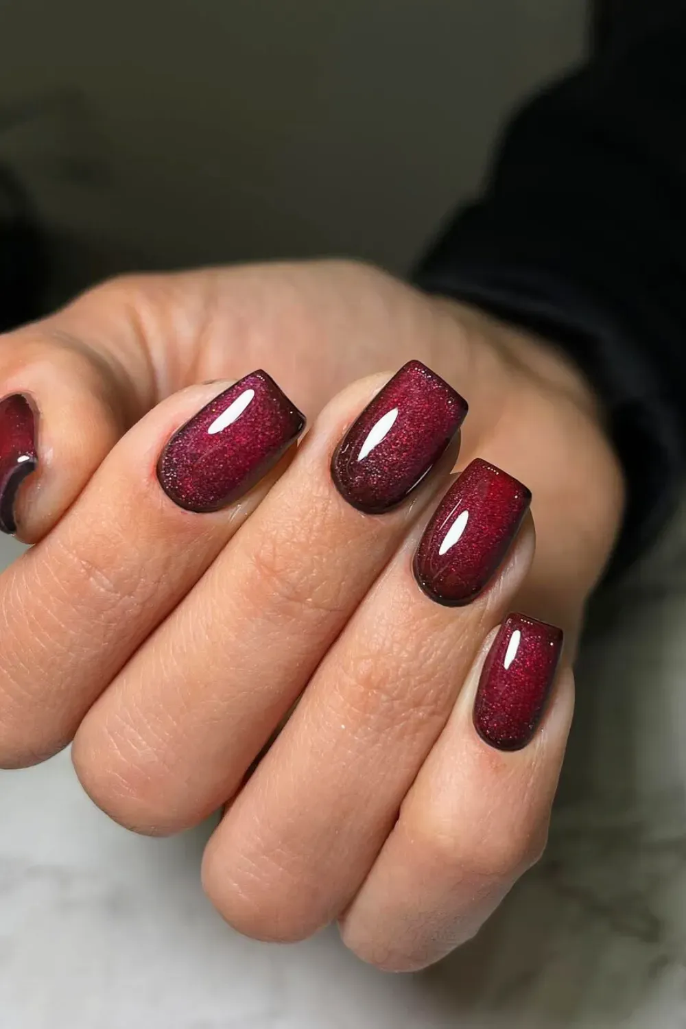 Short square nails in a deep crimson red polish featuring a magnetic cat-eye shimmer effect.