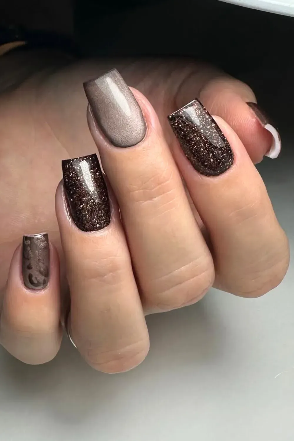 Square nails featuring alternating solid deep mocha polish and shimmering brown cat-eye glitter.