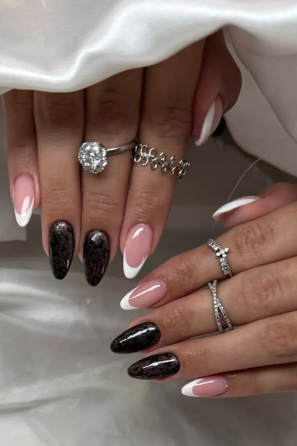 Almond nails with white French tips, dark brown glitter, and various rhinestone rings and charms.