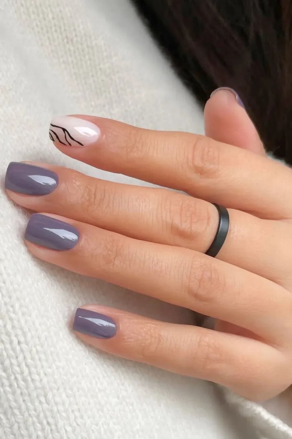 Moody Mauve with Abstract Line Art	Hand in a white sweater showing rounded nails in a dusty gray-purple, with one accent nail featuring black abstract wave lines on a white base.