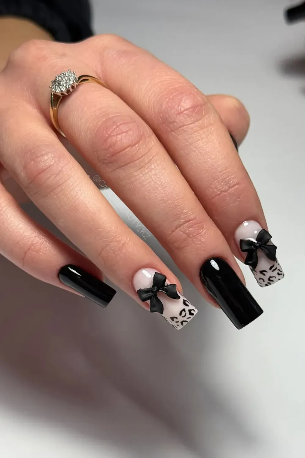 Black Coffin Nails with 3D Black Bows Long, glossy black coffin nails with two accent nails featuring a pink/nude base, leopard print tips, and prominent 3D black ribbon bow embellishments