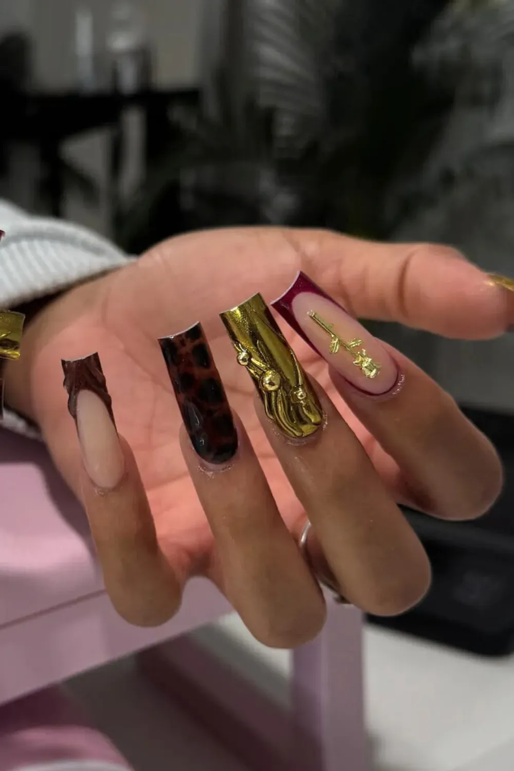 Long square nails featuring 3D gold abstract waves, dark leopard print, and deep burgundy French tips.