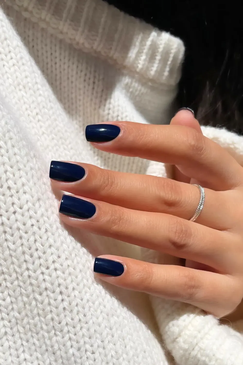 Chic Navy Blue Short Manicure	Hand holding a white sweater, showing short, rounded-square nails in a solid, glossy navy blue polish.
