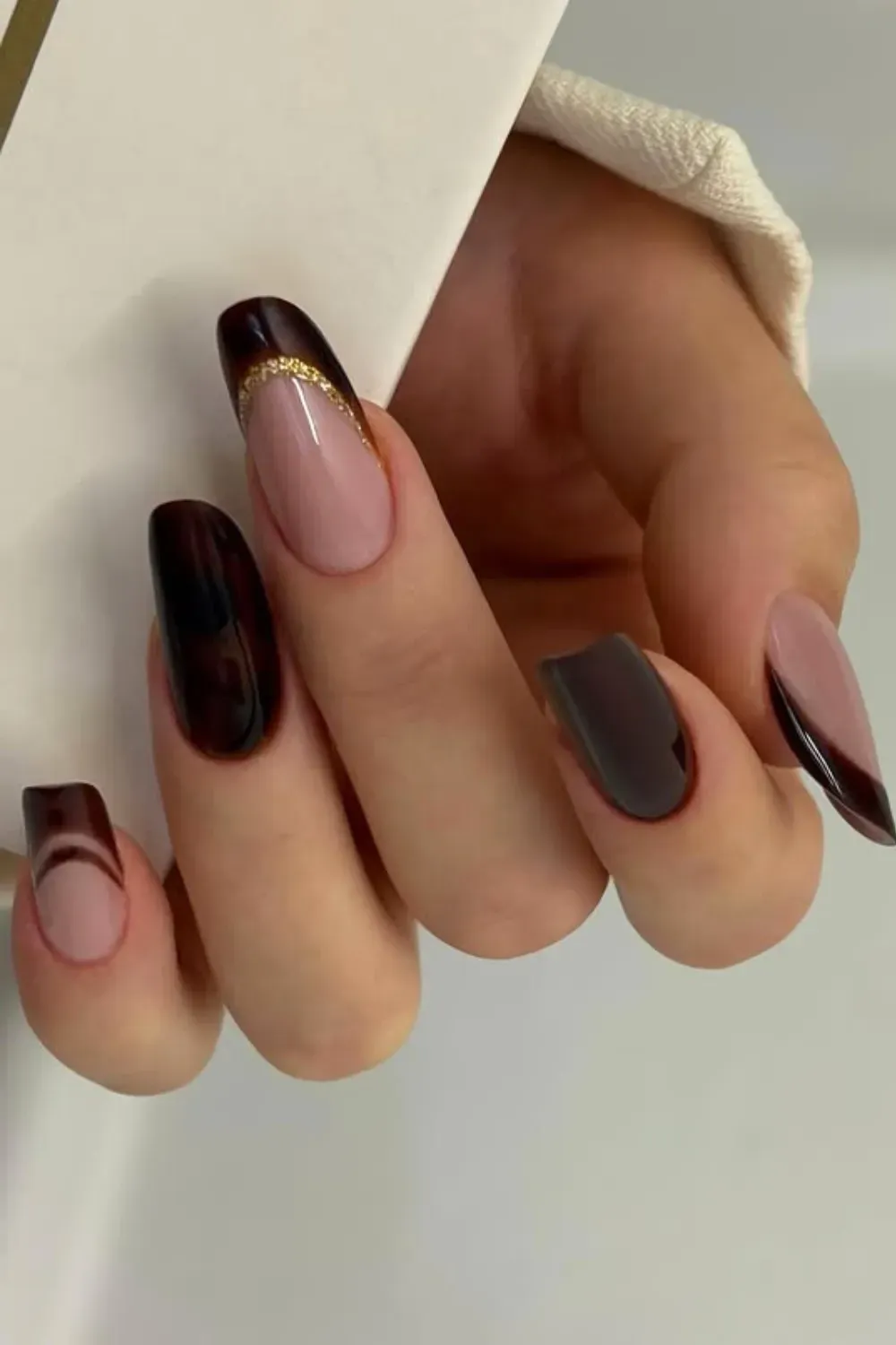 Gold 3D Charm Brown French Tip Nails Extra-long, square-tapered nails with brown and taupe V-tips, liquid gold contours, and 3D floral and abstract gold metal charms.