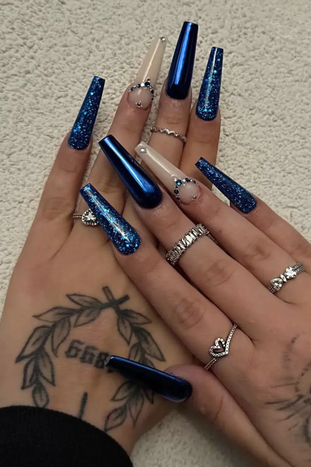 Long stiletto nails featuring royal blue glitter and metallic chrome, adorned with delicate clear rhinestones.