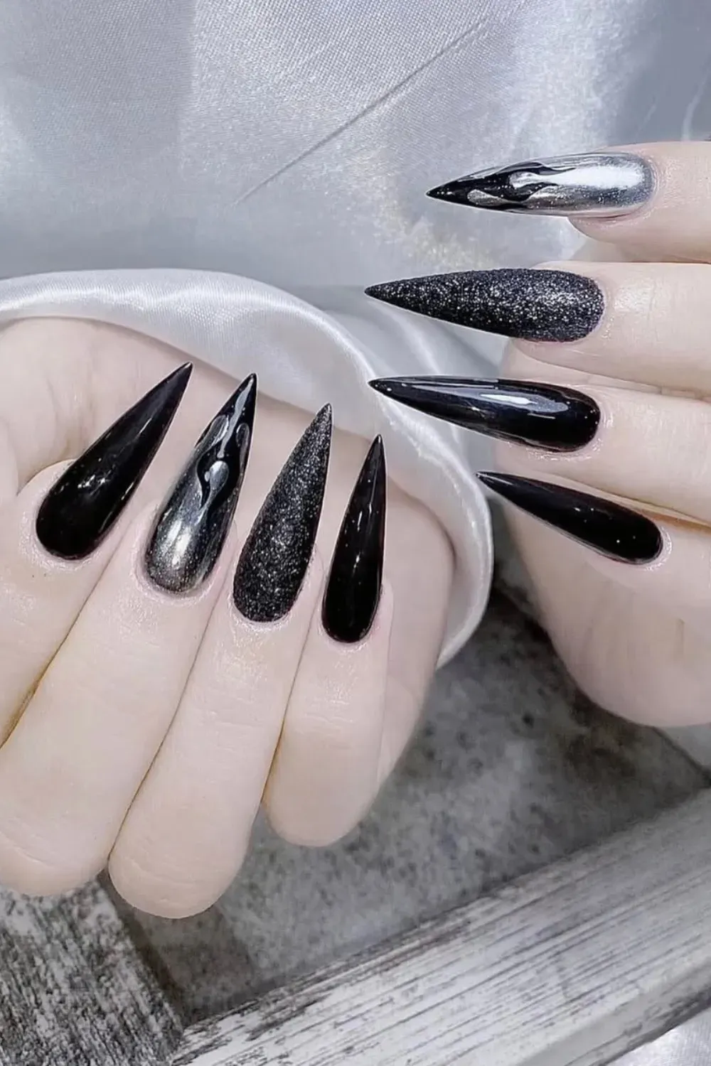 Stiletto nails featuring a mix of glossy black, black glitter, and metallic silver chrome polish.