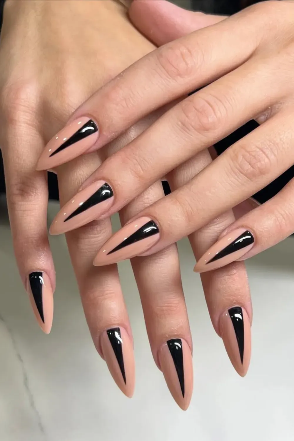  Stiletto nails with nude base featuring a glossy black geometric triangle shape pointing up from the tip. Stiletto nails with nude base featuring a glossy black geometric triangle shape pointing up from the tip.