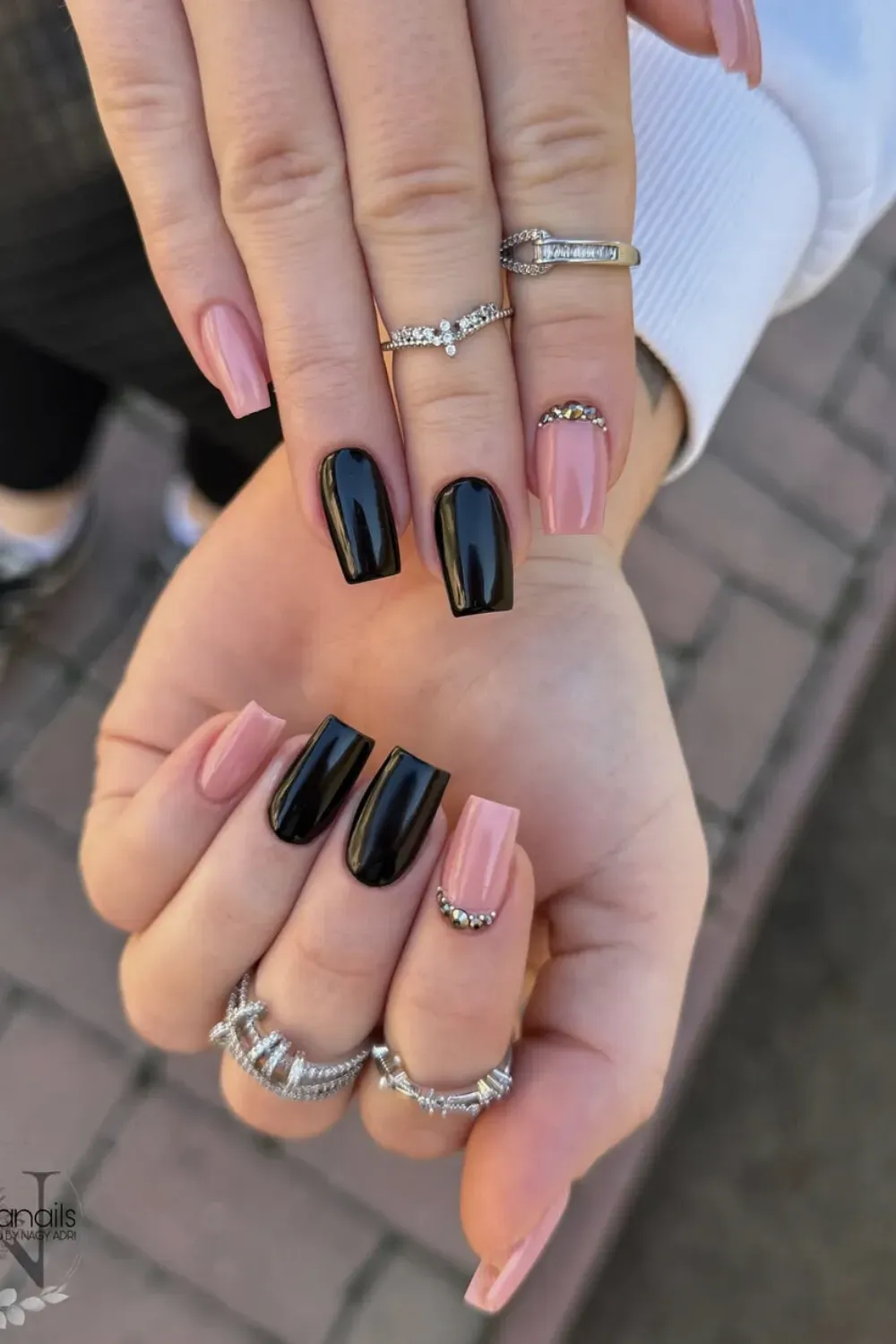 Square nails featuring a mix of soft pink and glossy black polish, with subtle rhinestone embellishments.