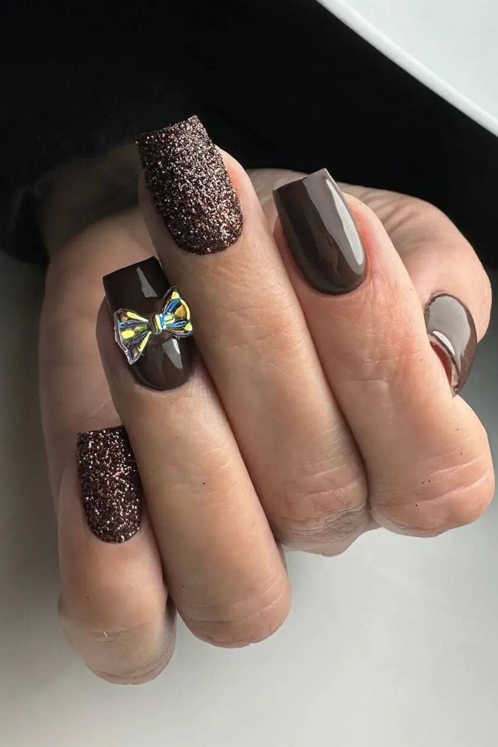  Square nails in dark chocolate brown and brown glitter, accented with an iridescent bow charm.