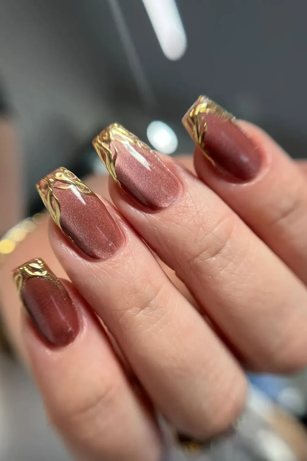 Rusty Red and Gold Foliage - Square-shaped nails with a rusty-red shimmering base and decorative gold foil resembling foliage along the tip, creating a French-style design.