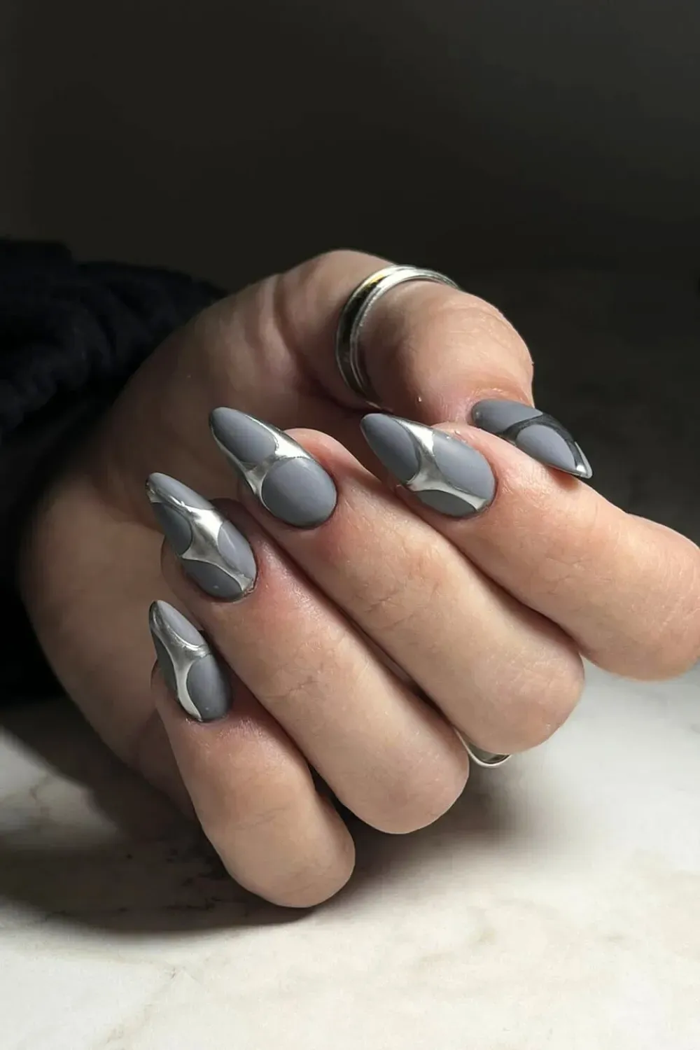 Almond nails in matte grey polish with raised, sculpted abstract shapes in liquid silver chrome.