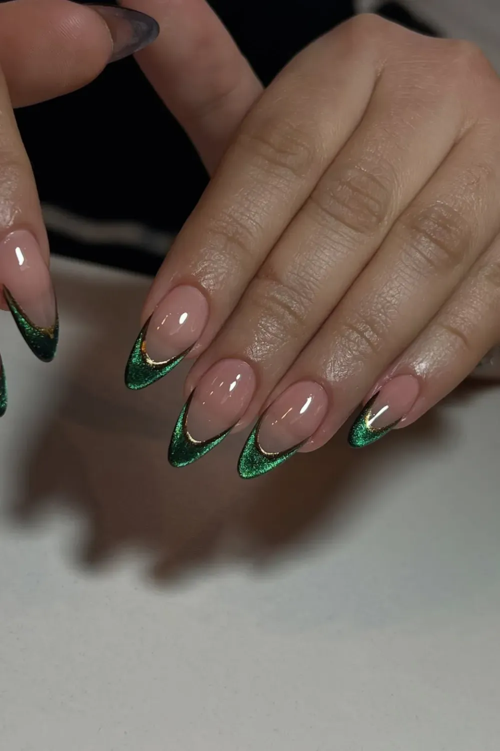 The Deep Forest French - Oval nails with a nude base and dramatic V-shaped tips in shimmering emerald green cat eye polish, accented with a thin gold line.