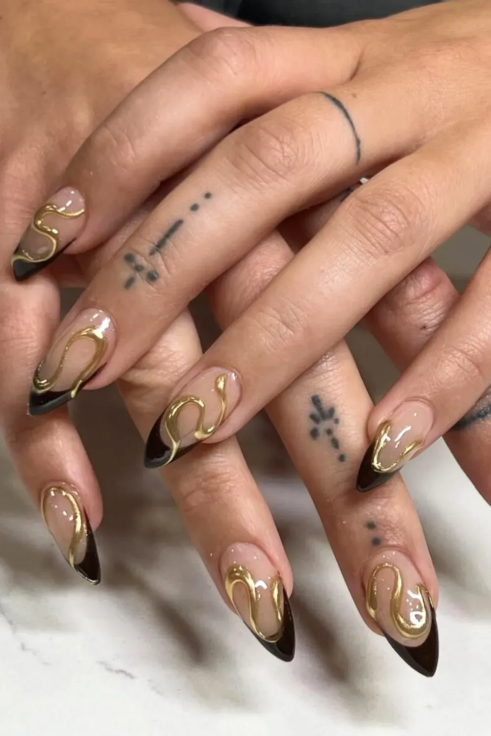 Almond nails with nude base and black tips, adorned with a raised 3D gold serpentine line design.