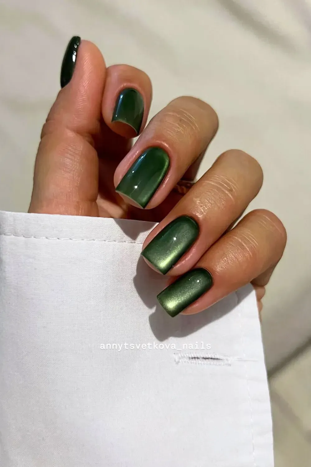 Mesmerizing Green Cat-Eye Nails	Hand in a white shirt cuff showing green square nails with a reflective, shifting cat-eye effect.