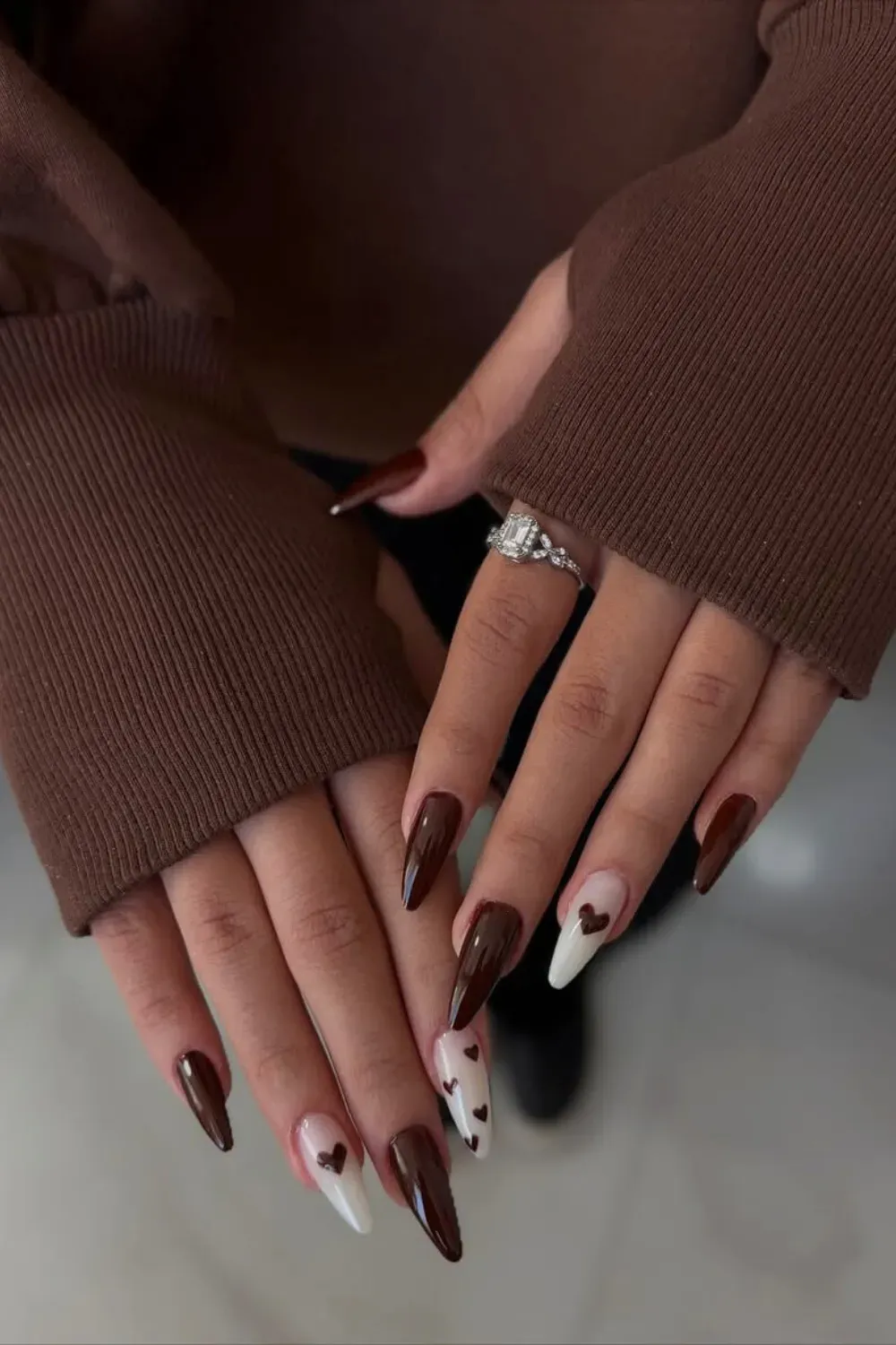 Dark Stiletto Nails with White Heart Accents Long, glossy stiletto nails in a deep, dark chocolate brown, featuring accent nails with a sheer white base and tiny black/brown heart patterns.